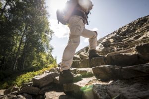 Mann wandert über Steine mit einem Rucksack einen Hügel hinauf