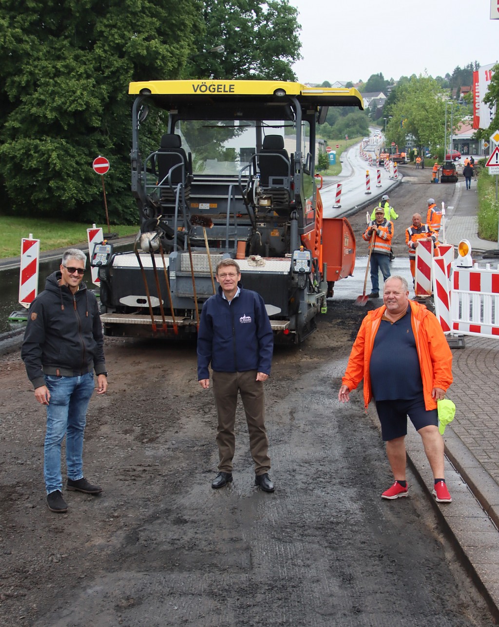 Die letzte Asphalt-Deckschicht wird gerade aufgebracht - dann ist die August-Balthasar-Straße fertig. Bürgermeister Peter Klär (Mitte) mit dem städtischen Tiefbauingenieur Daniel Fuchs (links) sowie Projektleiter Hans-Jürgen Schneider.