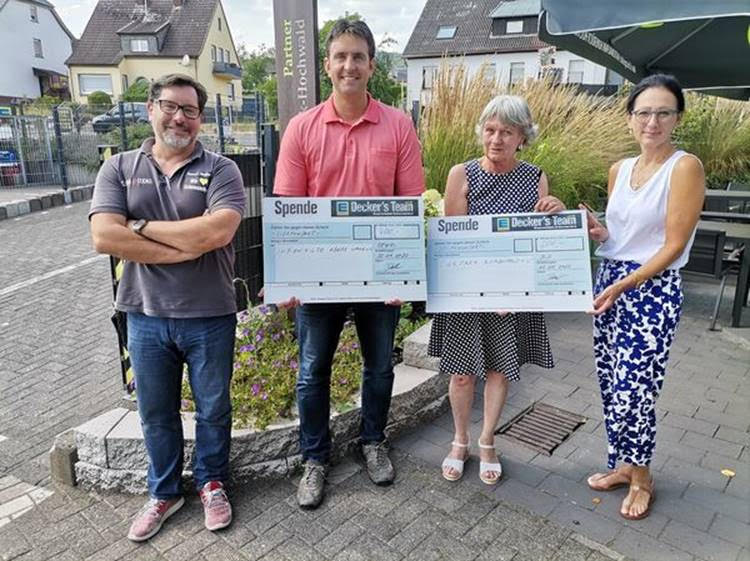 Symbolische Scheck-Übergabe, zwei Männer und zwei Frauen halten große Symbolische Schecks in die Kamera