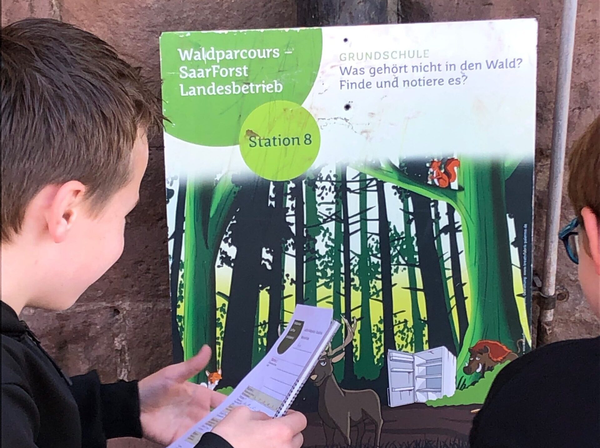 zwei schüler schauen auf einem flyer im wald