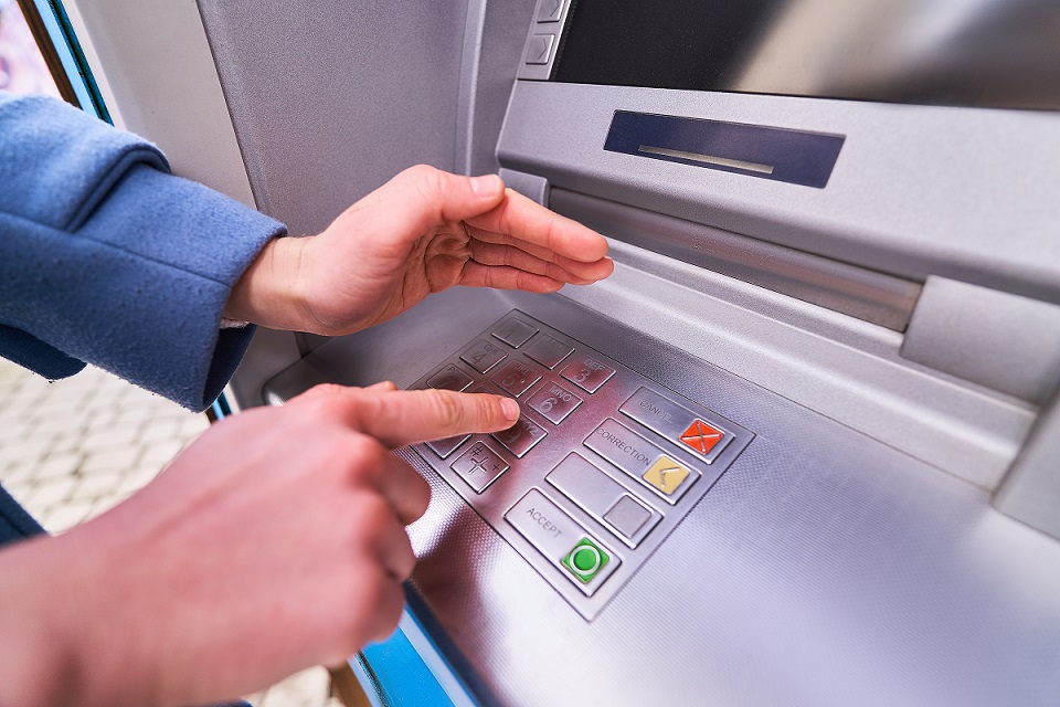 Person wählt und versteckt mit der anderen Hand zur Sicherheit einen PIN-Code auf der Tastatur eines Geldautomaten, um Geld abzuheben