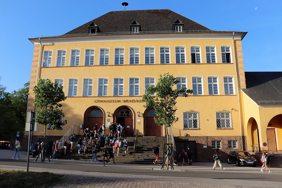 Ansicht des Schulgebäudes des Gymnasiums Wendalinum zeigt den Haupteingang, auf der Treppe zum Eingang befinden sich Schülerinnen und Schüler