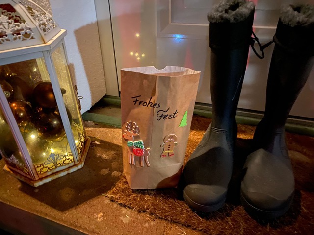 Vor einer Haustür stehen eine Geschenketüte und ein Paar Stiefel