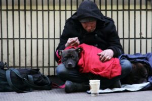 Ein Obdachloser sitzt auf der Straße und hält seinen Hund auf dem Schoß.
