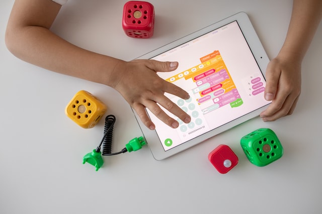Ein Kind (man sieht nur seine Arme) spielt mit einem Tablet. Daneben liegt Spielzeug.
