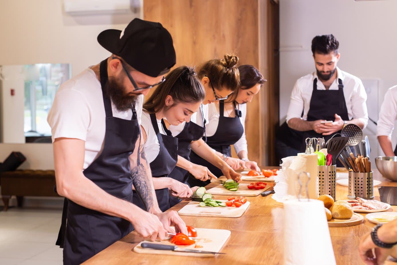 Cooking course - senior male chef in cook uniform teaches young people cooking class students to