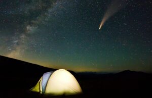 Tourist hikers tent in mountains at night with stars and Neowise comet