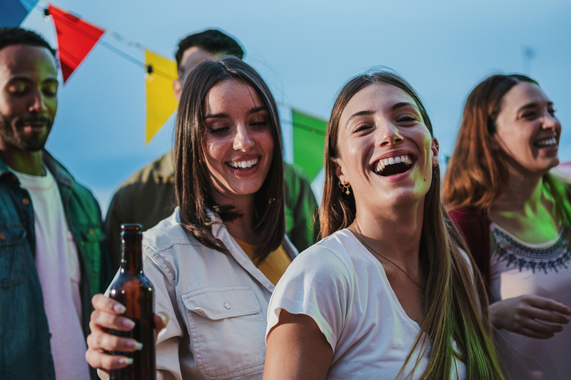 Two young women dancing and having fun with a happy group of best friends at music fest, enjoying