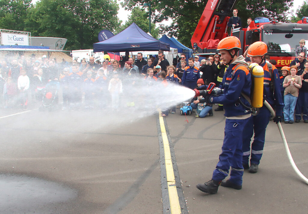 Mann mit Feurwehrschlauch und Brandschutzbekleidung löscht ein demonstratives Feuer